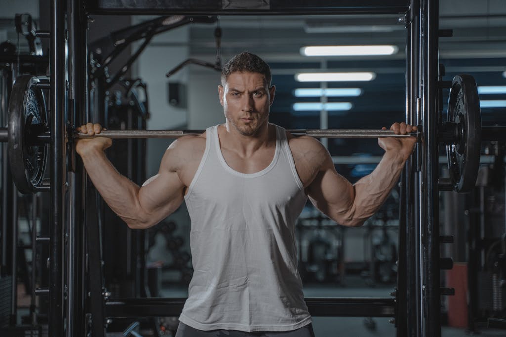 A strong, muscular man in a white tank top lifting weights in the gym.